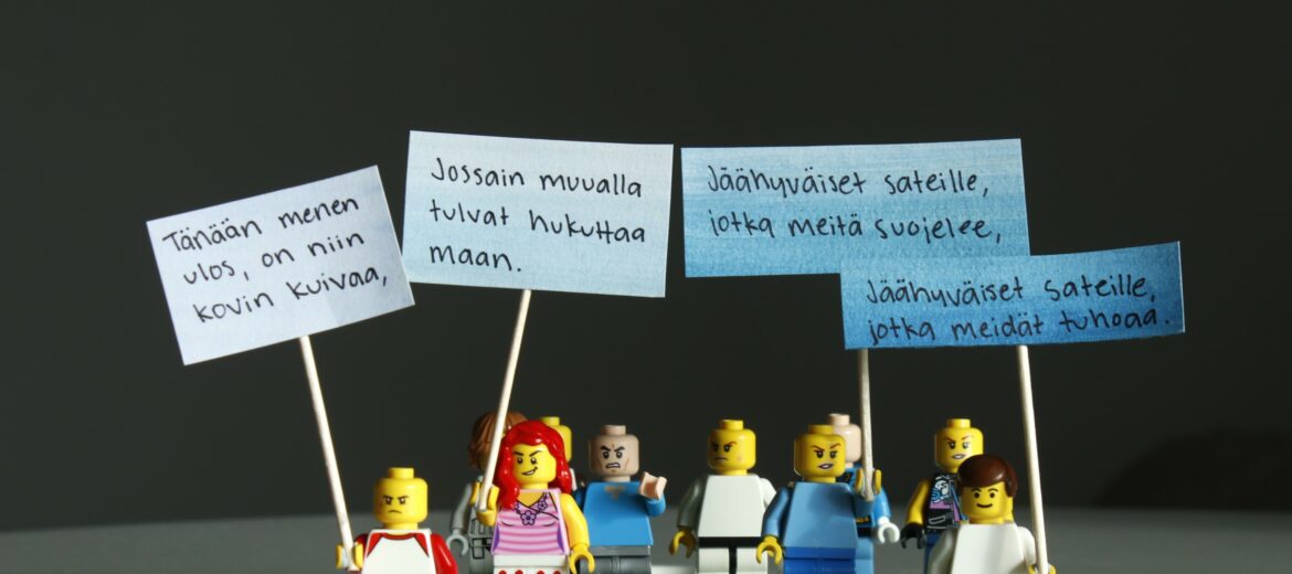 Ajatussepän teos. Kuvassa pienet lego-ukot on valokuvattu mielenosoituskyltit kädessä.